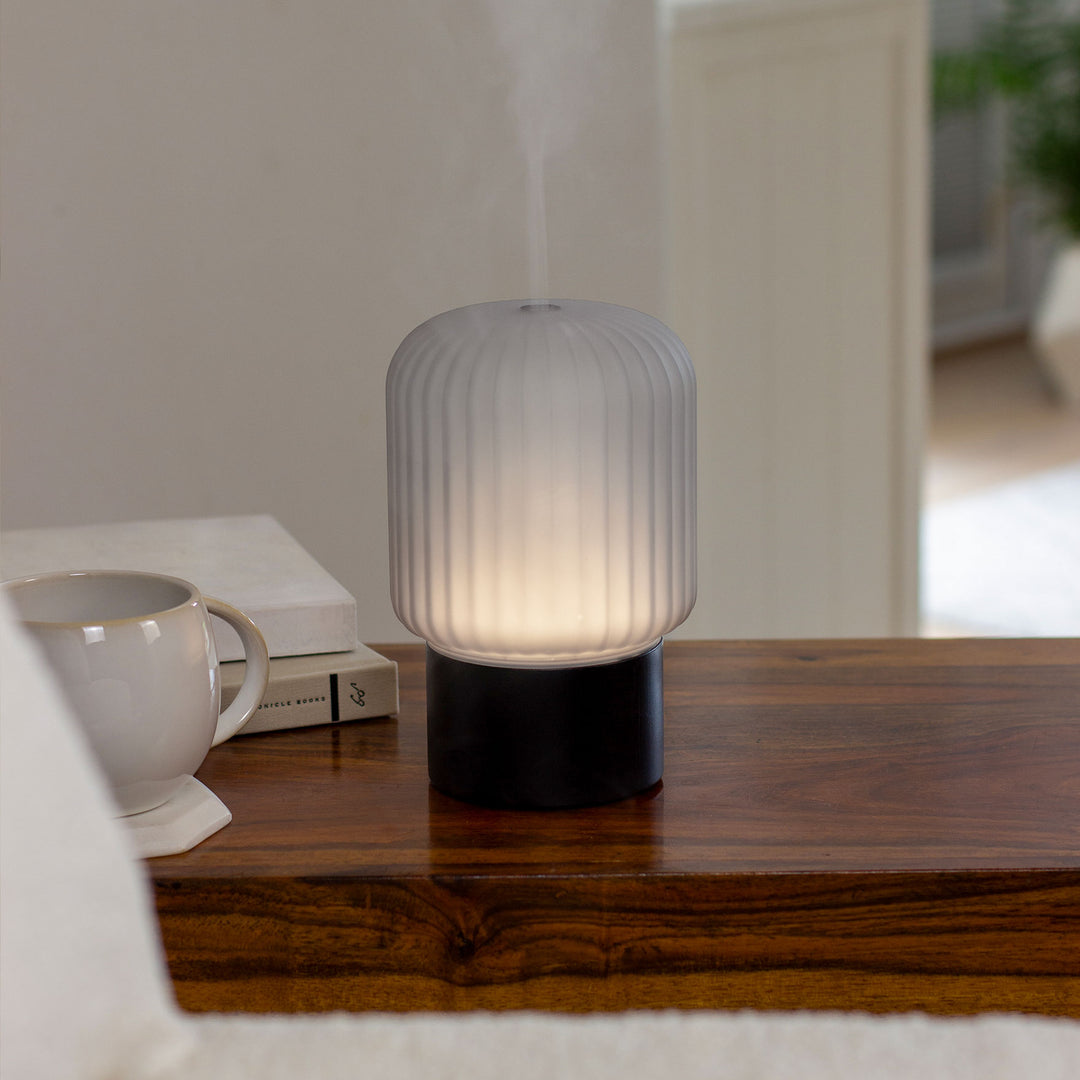 Made By Zen Atmo aroma diffuser emitting a fine mist on a wooden coffee table with soft ambient lighting in a contemporary living room.