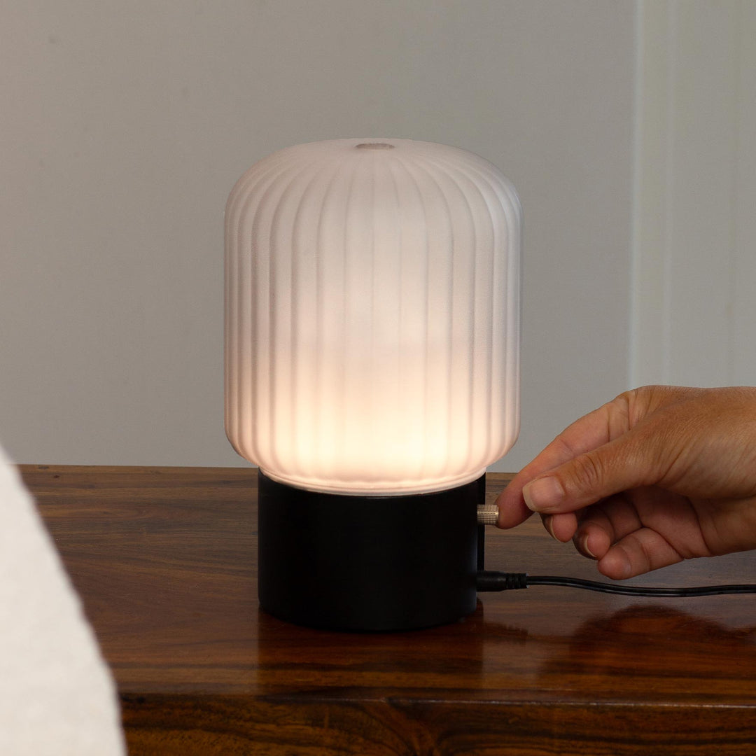 Made By Zen Atmo diffuser with glowing with warm light, shown on a wooden surface, with a hand turning the light dial.